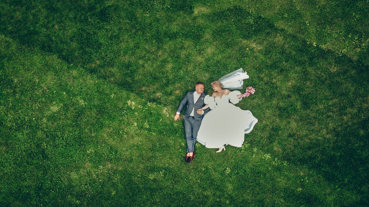 an aerial view of a bride and groom lying on grass